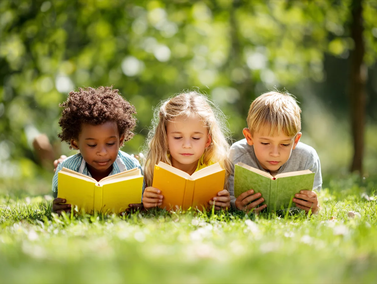 Three children reading books together on the grass